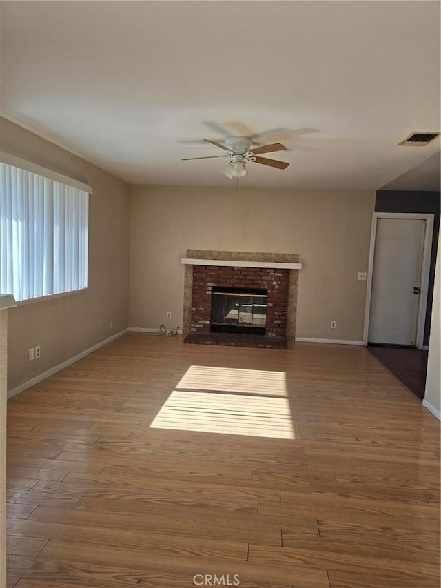 unfurnished living room with a ceiling fan, visible vents, wood finished floors, baseboards, and a brick fireplace