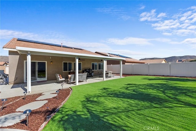 rear view of house with a lawn, a fenced backyard, a patio area, roof mounted solar panels, and stucco siding