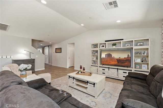 living area featuring lofted ceiling, visible vents, light wood-style flooring, and a barn door