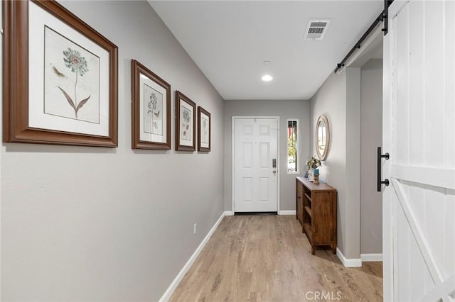 entryway featuring light wood-style floors, visible vents, baseboards, and a barn door