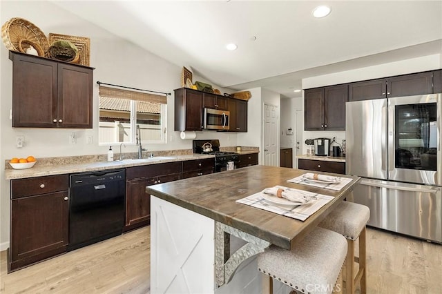 kitchen with light wood-style flooring, a center island, vaulted ceiling, black appliances, and a sink