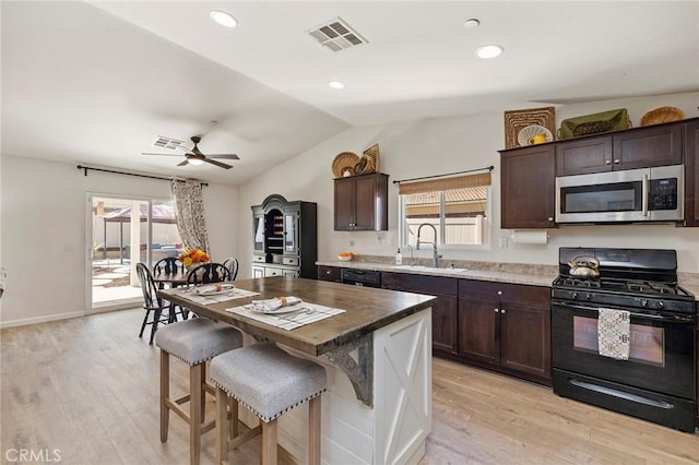 kitchen with black gas range, a sink, a kitchen island, visible vents, and stainless steel microwave