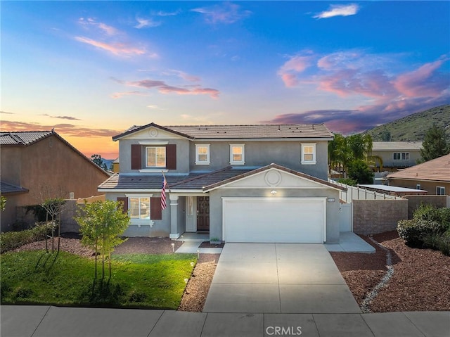 traditional-style home featuring driveway, a tiled roof, fence, and stucco siding