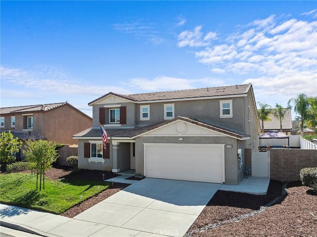 traditional-style home featuring fence, driveway, an attached garage, and stucco siding