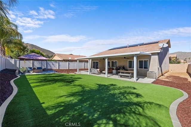 rear view of house featuring a patio, stucco siding, a gazebo, roof mounted solar panels, and a fenced backyard