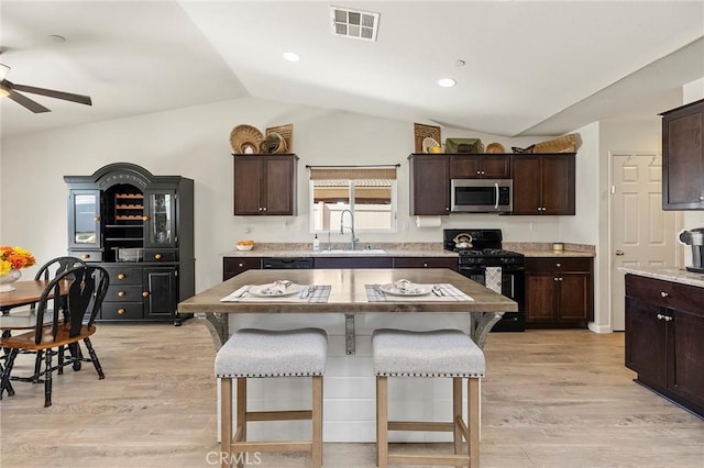 kitchen with visible vents, stainless steel microwave, black gas range oven, a kitchen island, and a sink