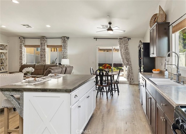 kitchen featuring visible vents, dark countertops, dark brown cabinets, white cabinetry, and a sink