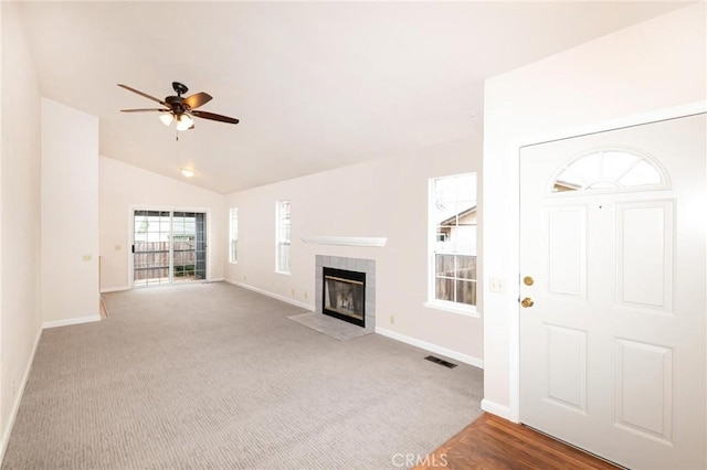 unfurnished living room with visible vents, a ceiling fan, vaulted ceiling, a tile fireplace, and baseboards