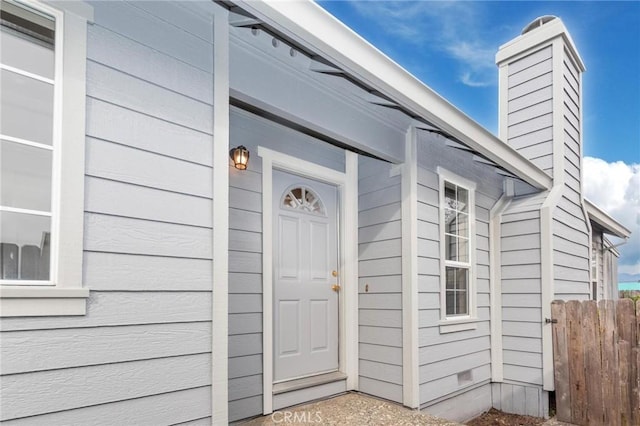 view of exterior entry with crawl space, fence, and a chimney