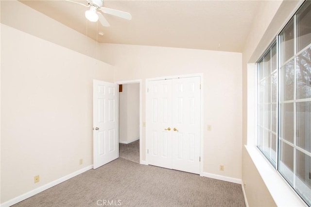 unfurnished bedroom featuring lofted ceiling, multiple windows, baseboards, and light colored carpet