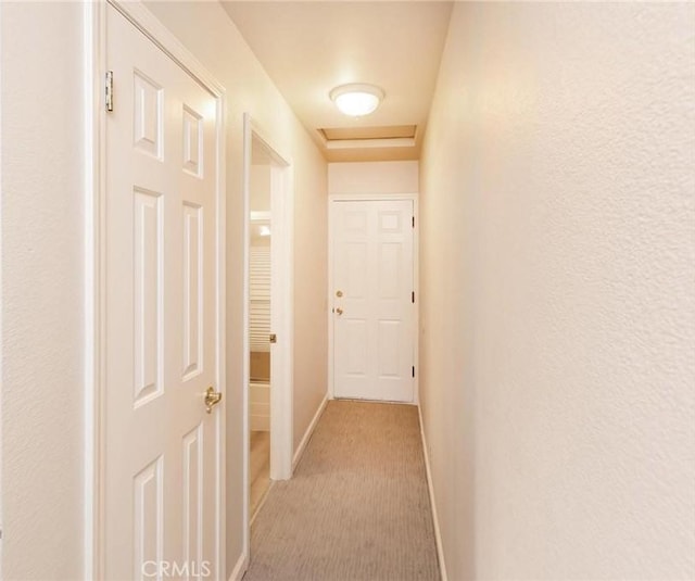 hall featuring light carpet, attic access, and baseboards