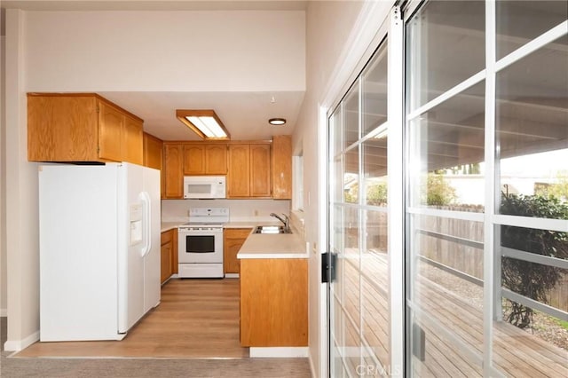 kitchen with brown cabinets, light countertops, light wood-style flooring, a sink, and white appliances