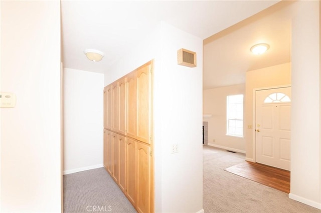 hallway with light carpet, visible vents, and baseboards