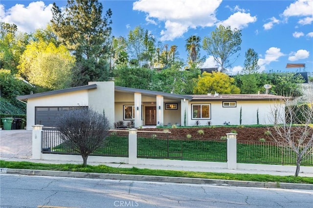 view of front of home featuring driveway, a fenced front yard, an attached garage, and stucco siding