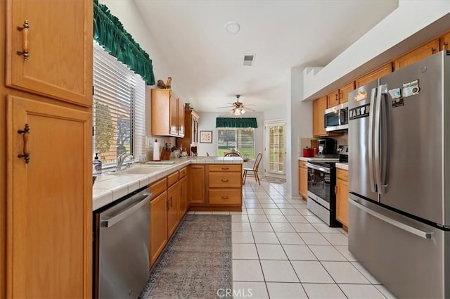 kitchen featuring light tile patterned flooring, a peninsula, a sink, appliances with stainless steel finishes, and tile counters