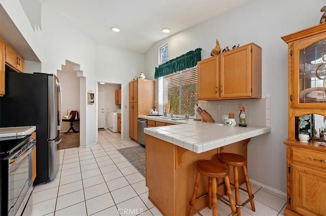 kitchen with tile countertops, appliances with stainless steel finishes, a kitchen breakfast bar, a peninsula, and backsplash