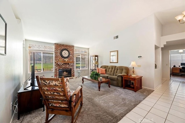 living room featuring light tile patterned floors, light colored carpet, visible vents, a towering ceiling, and a brick fireplace