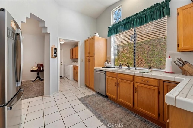 kitchen with stainless steel appliances, brown cabinetry, light tile patterned flooring, and tile counters