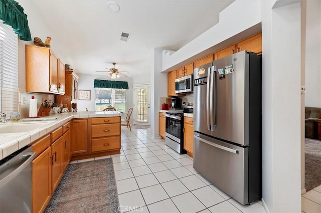 kitchen with tile countertops, light tile patterned floors, stainless steel appliances, visible vents, and a peninsula