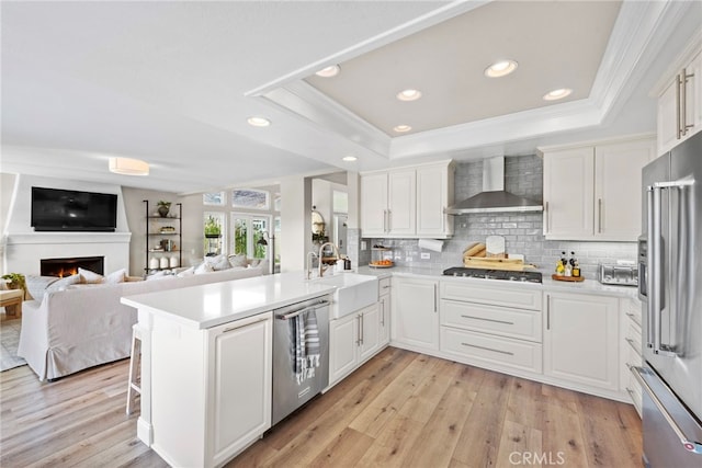 kitchen with stainless steel appliances, light countertops, wall chimney range hood, and a peninsula