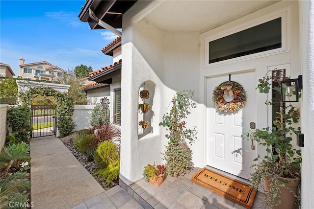 doorway to property with a gate, a tile roof, fence, and stucco siding