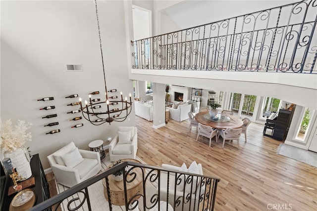 living area featuring a warm lit fireplace, a high ceiling, wood finished floors, and visible vents