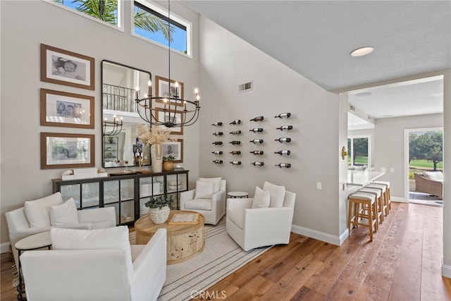 living area with baseboards, visible vents, a towering ceiling, wood finished floors, and a notable chandelier