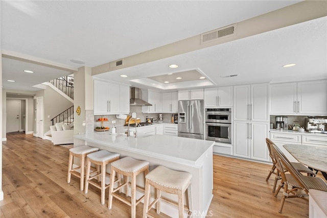 kitchen featuring stainless steel appliances, wall chimney range hood, a breakfast bar area, and white cabinets