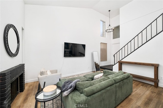 living room with a fireplace, wood finished floors, baseboards, stairway, and an inviting chandelier