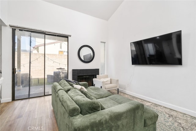 living room with high vaulted ceiling, a fireplace, baseboards, and wood finished floors