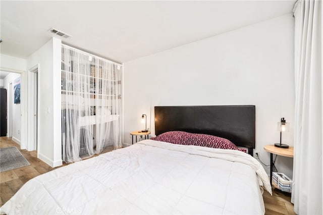 bedroom with wood finished floors, visible vents, and baseboards