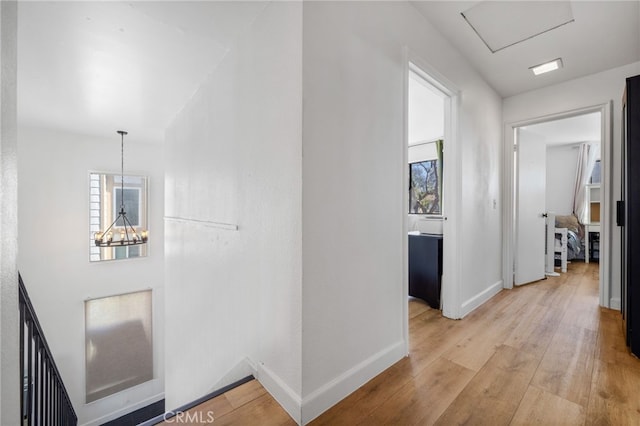 corridor with light wood finished floors, baseboards, and a notable chandelier