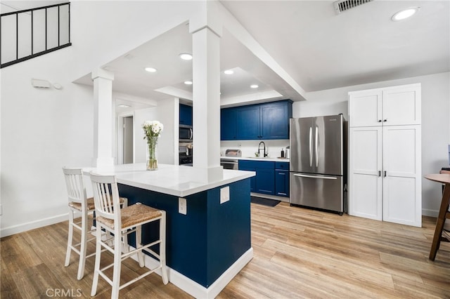 kitchen with a breakfast bar area, blue cabinets, appliances with stainless steel finishes, light wood finished floors, and decorative columns