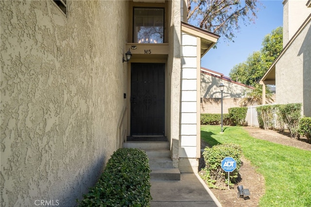 property entrance featuring fence, a lawn, and stucco siding