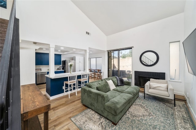 living area featuring baseboards, visible vents, dark wood finished floors, a fireplace, and high vaulted ceiling