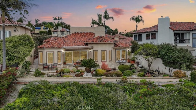 back of house at dusk with a tiled roof, a patio area, and stucco siding