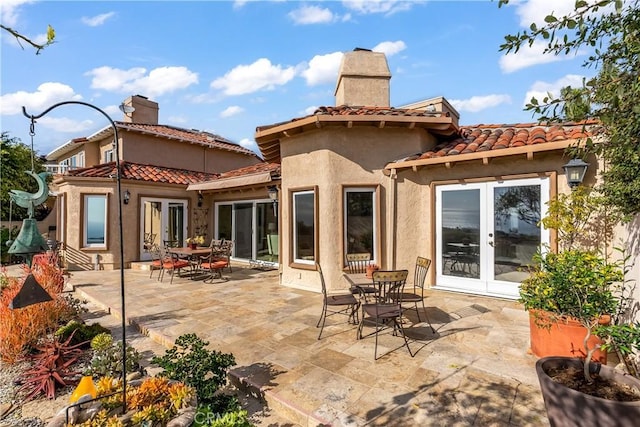 rear view of property featuring a tile roof, a chimney, french doors, a patio area, and stucco siding