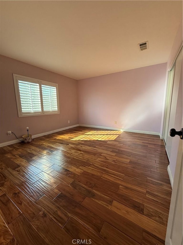 empty room featuring dark wood-style floors, visible vents, and baseboards