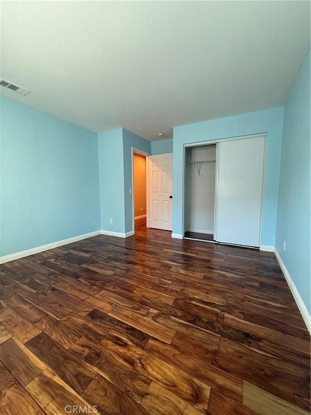 unfurnished bedroom featuring a closet, dark wood-style flooring, visible vents, and baseboards