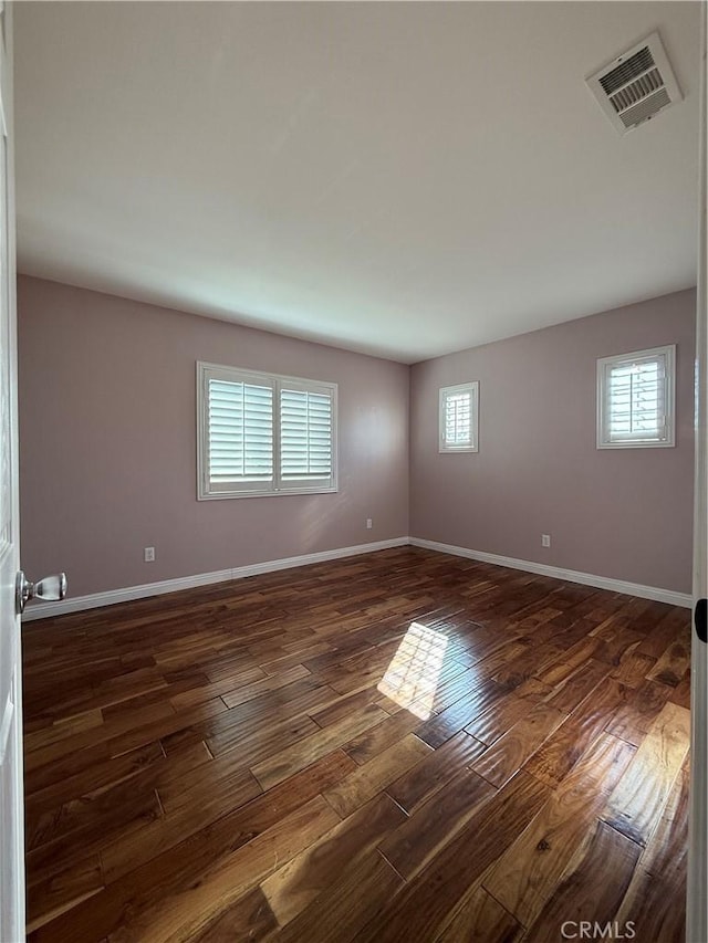 empty room featuring dark wood-style floors, baseboards, and visible vents