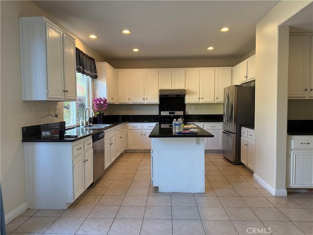 kitchen featuring stainless steel appliances, a sink, a kitchen island, white cabinetry, and dark countertops