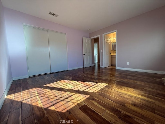 unfurnished bedroom with connected bathroom, dark wood-type flooring, visible vents, baseboards, and a closet