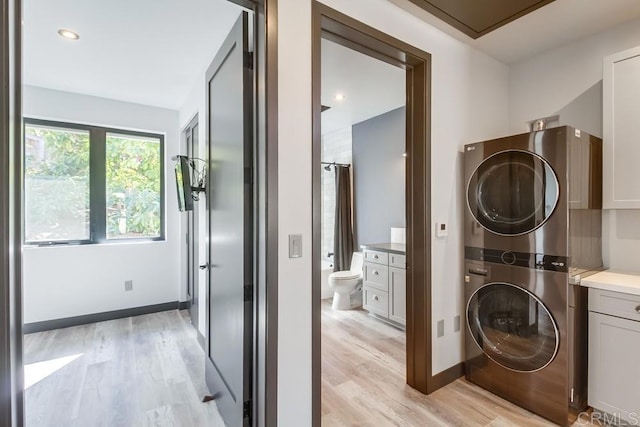 laundry room with baseboards, stacked washer and dryer, and light wood-style floors