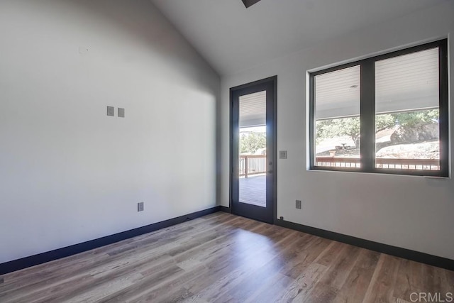 empty room featuring vaulted ceiling, wood finished floors, and baseboards