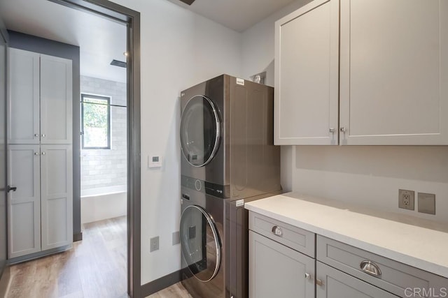 laundry room with cabinet space, light wood finished floors, and stacked washer / drying machine