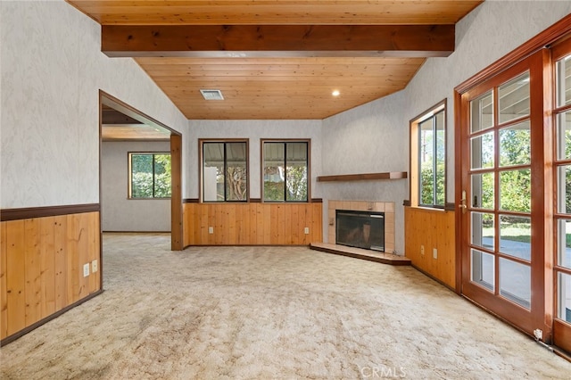 unfurnished living room with a tile fireplace, light carpet, wood walls, wainscoting, and beamed ceiling