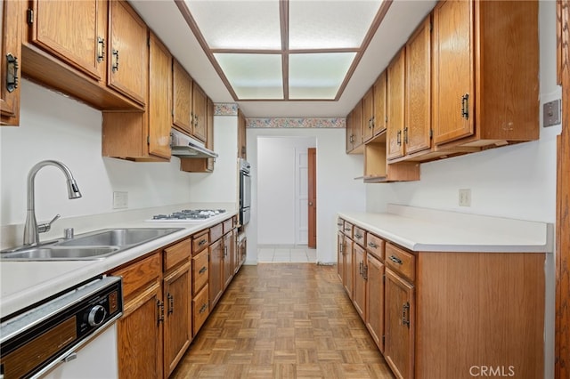 kitchen with light countertops, brown cabinetry, a sink, white appliances, and under cabinet range hood