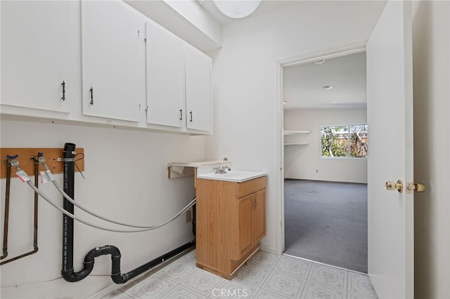 laundry room featuring cabinet space, a sink, light carpet, and baseboards