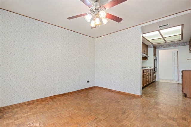 unfurnished room featuring visible vents, a ceiling fan, ornamental molding, baseboards, and wallpapered walls