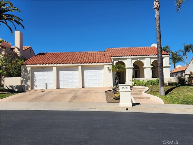 mediterranean / spanish-style home with a garage, a tiled roof, concrete driveway, and stucco siding